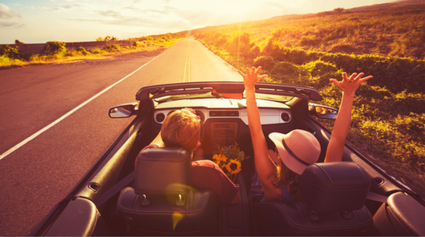 A couple driving in a car on highway toward a sunset.