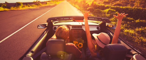 Car with driver and passenger riding into a sunset.